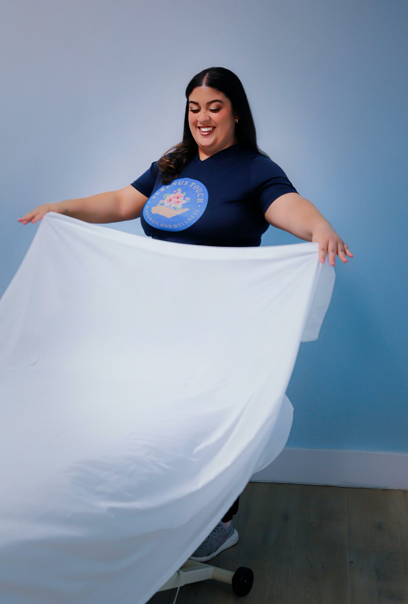 Woman holding a large white sheet, smiling, standing against a blue background.