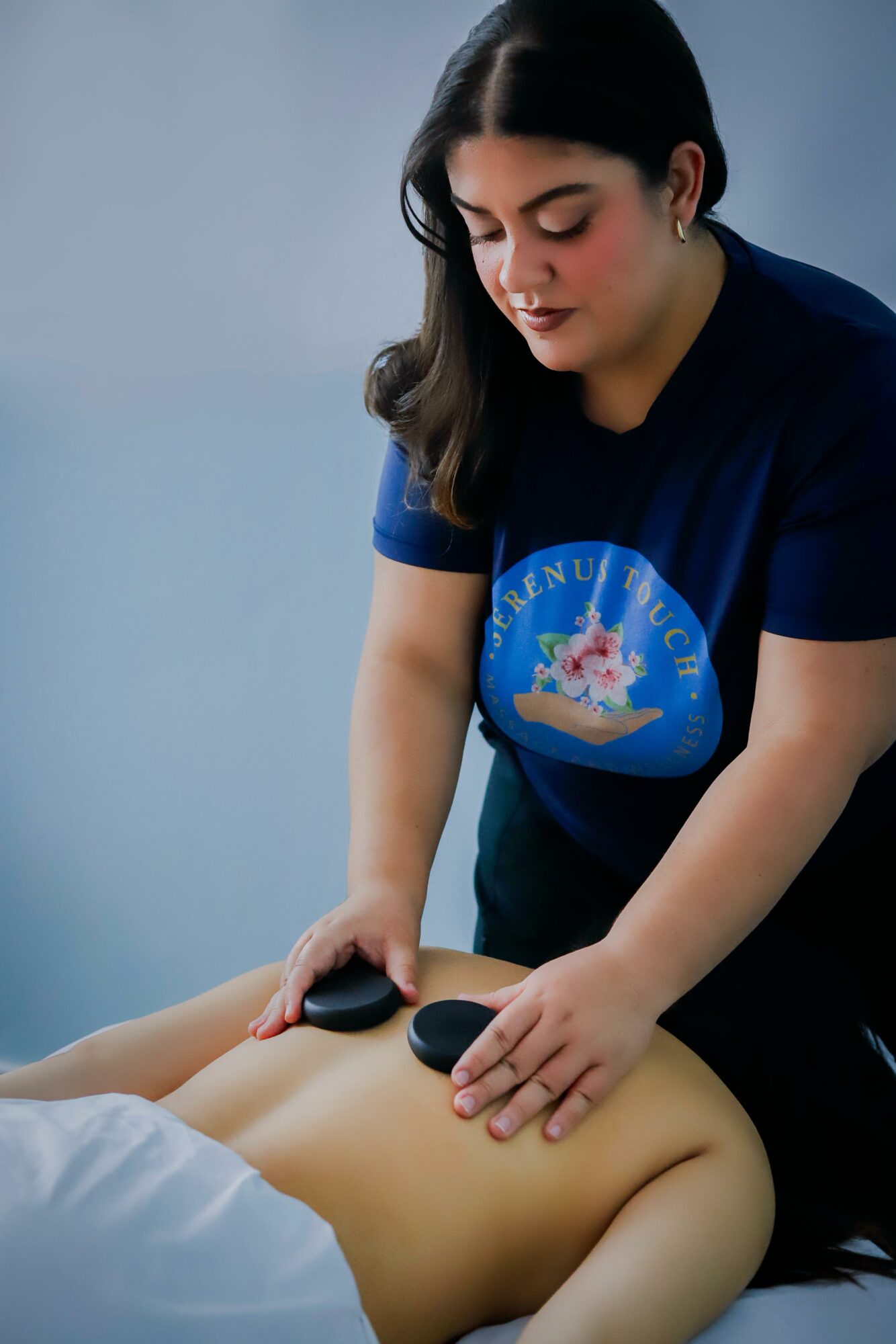 Woman giving a massage to a person lying face down, focusing on their back, against a plain background.