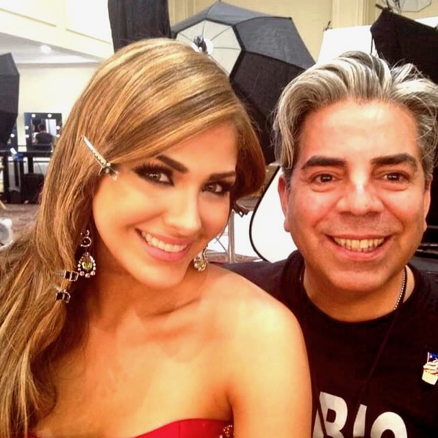 A smiling woman with long hair and earrings, and a smiling man with gray hair, in a studio setting.