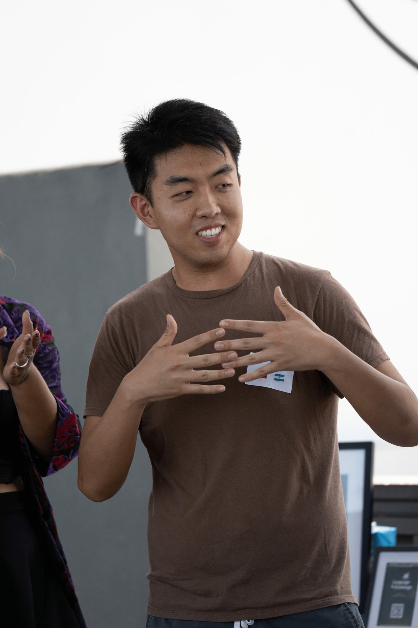 Young man speaking with hands on chest, smiling, in a casual setting.