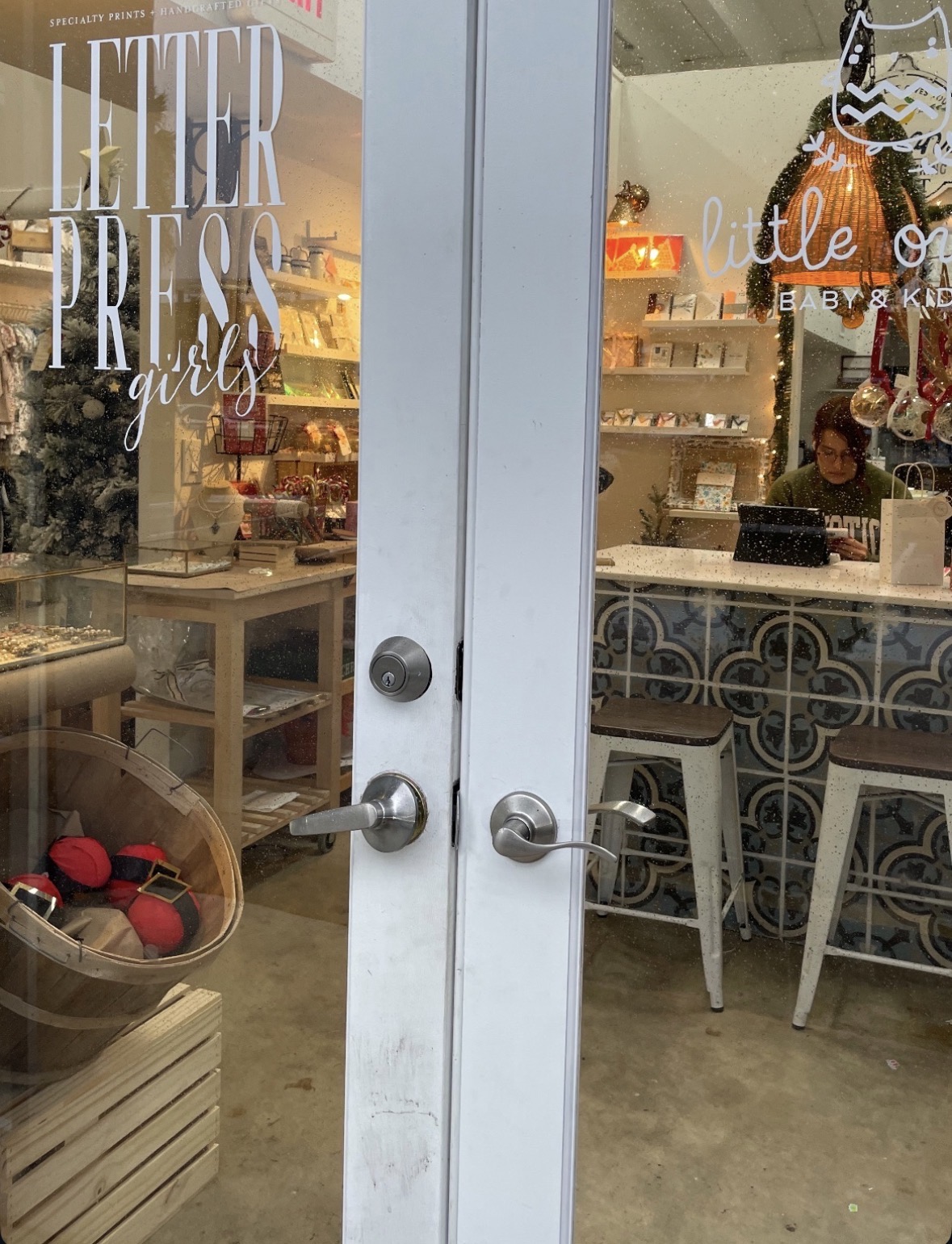 Glass door with store interior visible, including shelves, a person working, and decorative items, with text on the door reading 'Letterpress girls'.