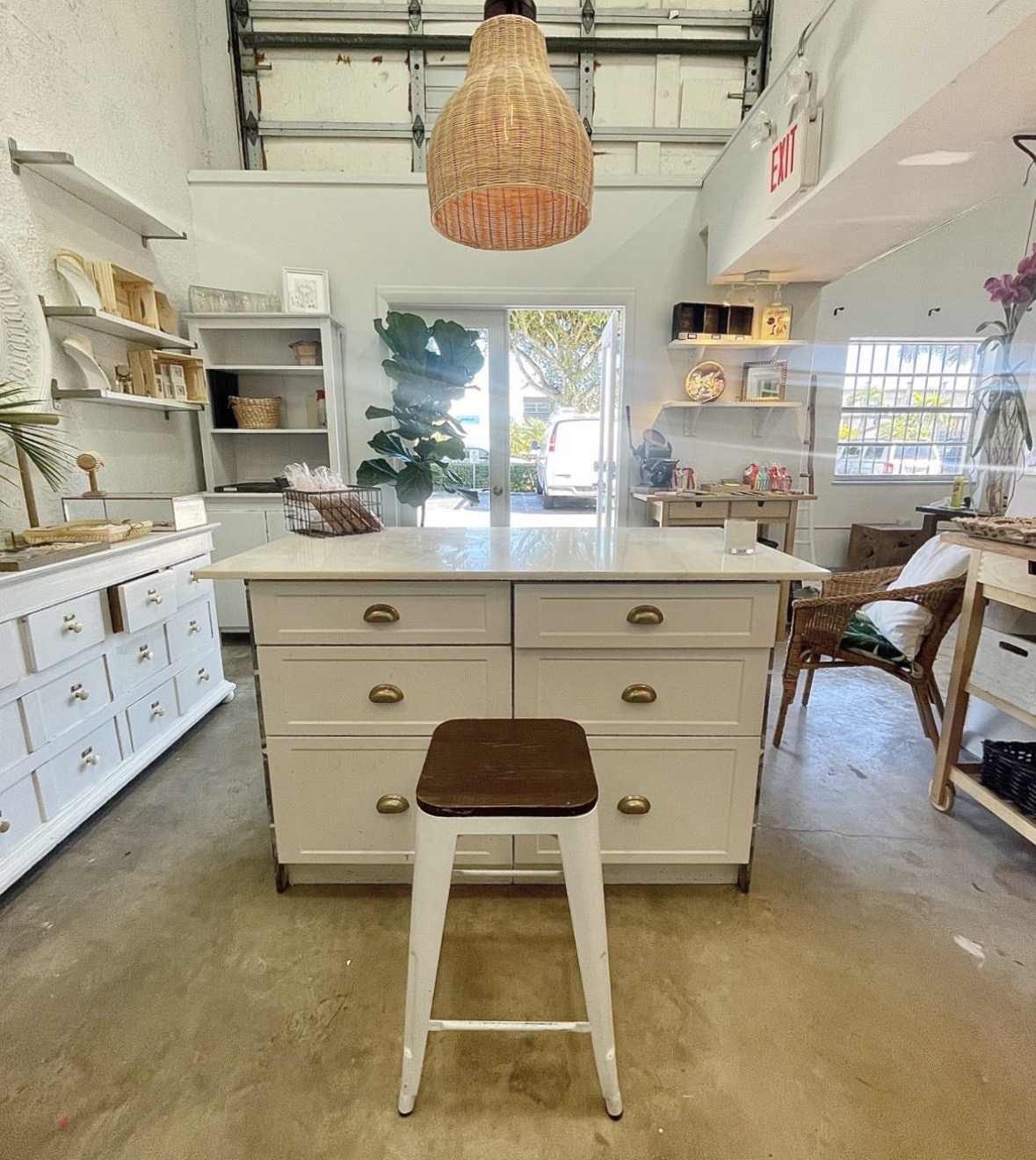 Interior of a store with a white island counter, a stool, shelves, and a large hanging light fixture.