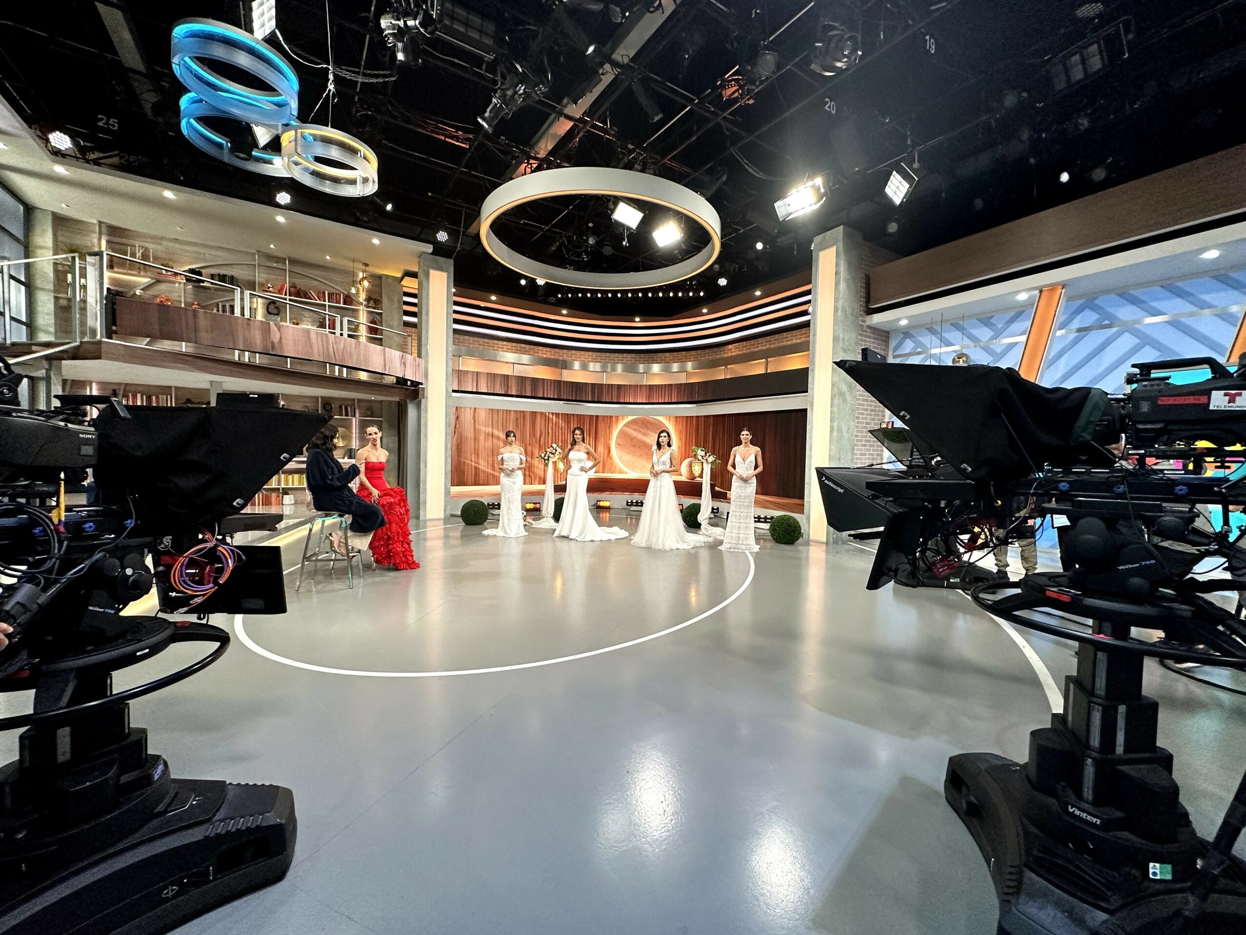 Television studio with a circular stage, cameras, and people in formal attire, with modern lighting and set design.