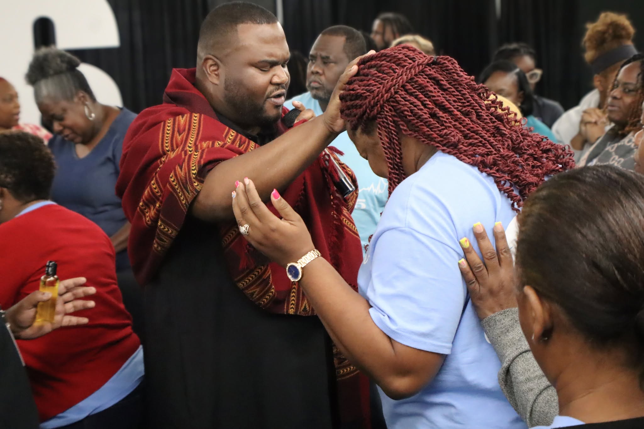 Two people are engaged in a prayer or blessing, with others observing in the background.
