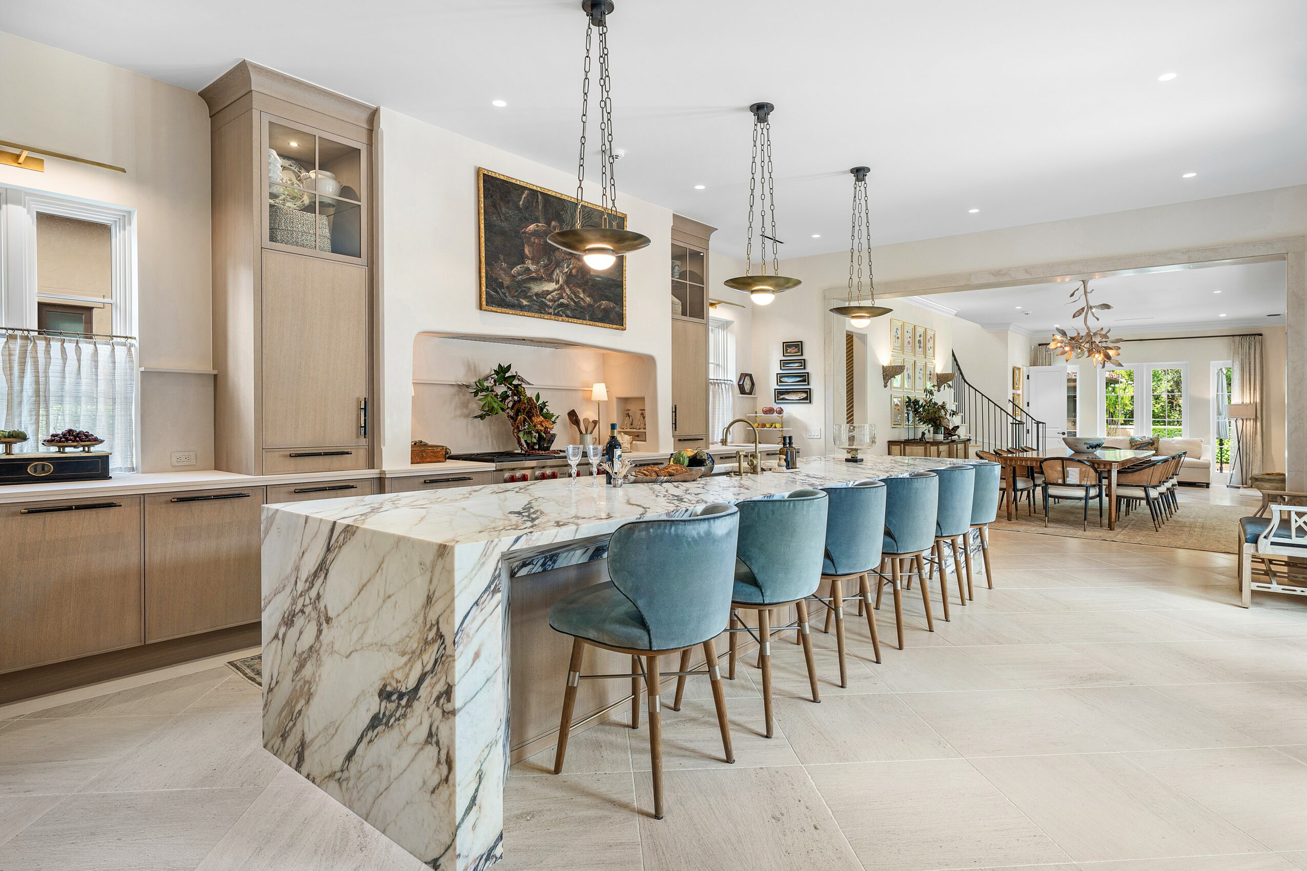 Modern kitchen with marble island, blue chairs, and open dining area in bright, spacious home.