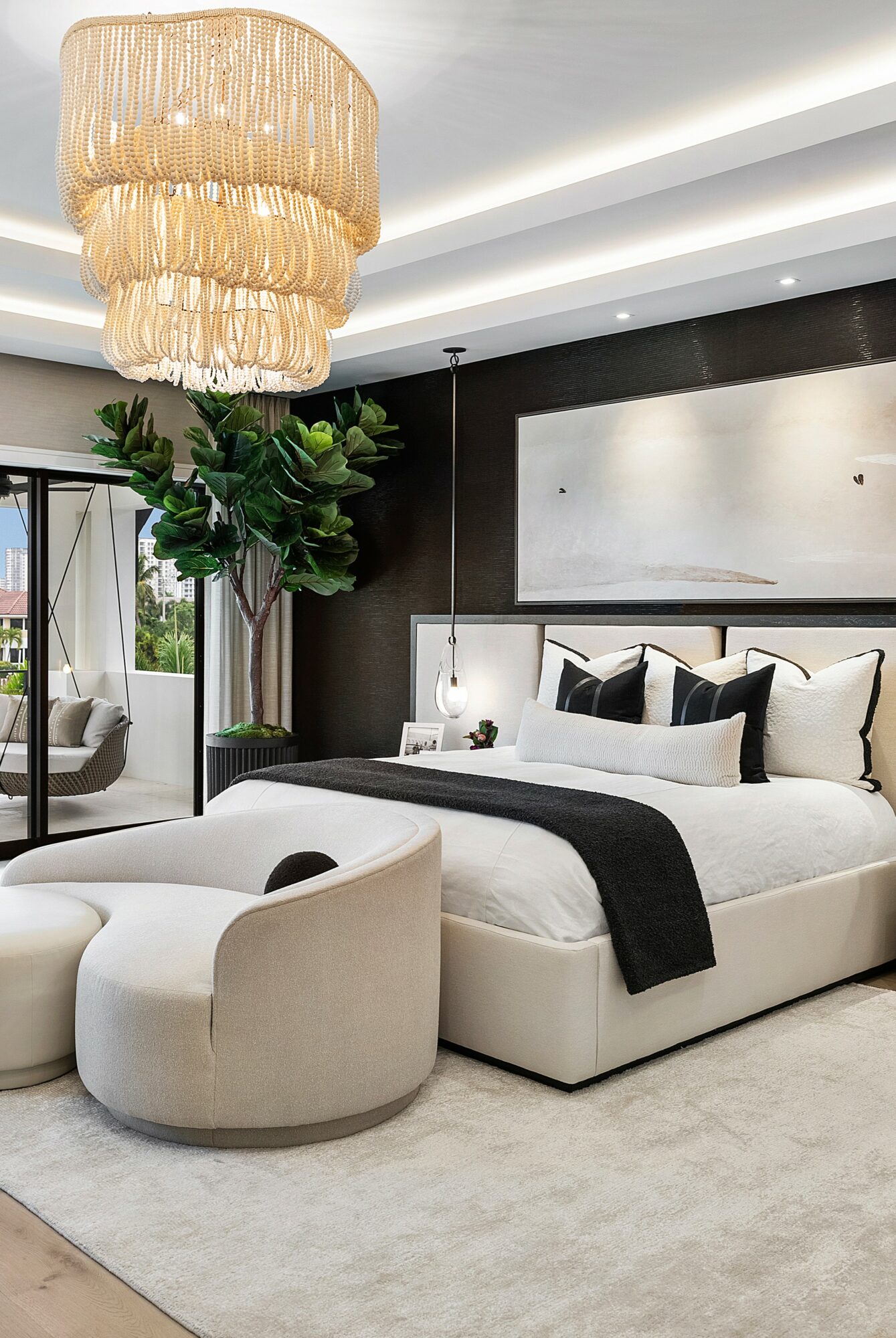 Modern bedroom with a large bed, black and white bedding, a chandelier, and a potted plant in the corner.