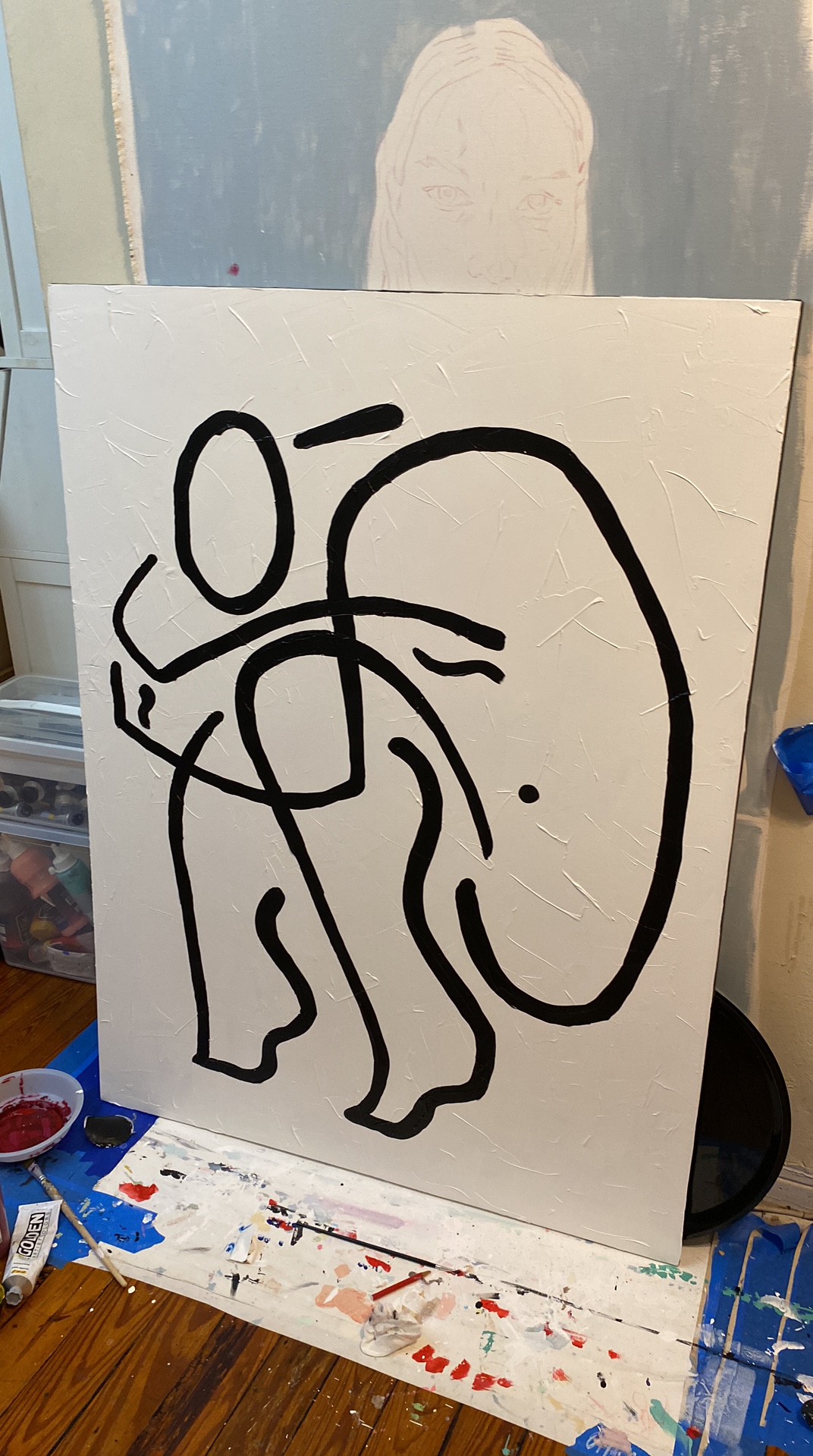 Black abstract line drawing on white paper, resembling a stylized face or figure, placed on a table with art supplies.