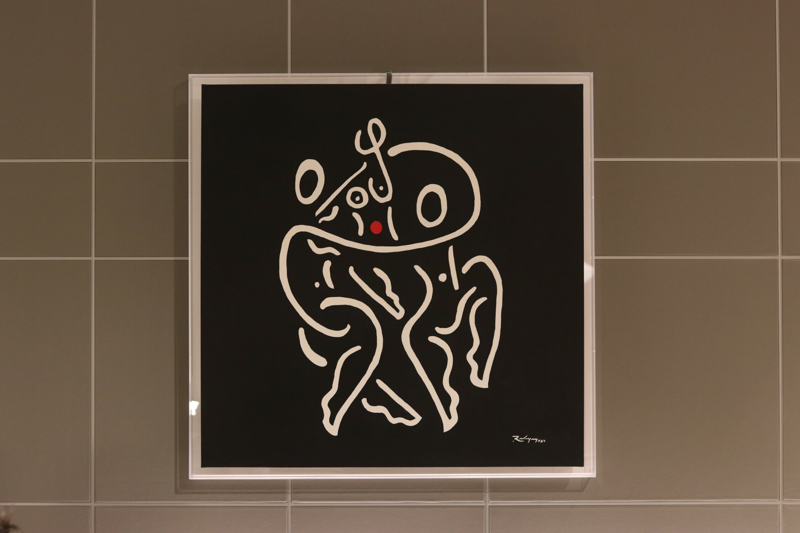 Abstract line drawing of two dancing figures on a black background, with a small red accent, framed on a tiled wall.