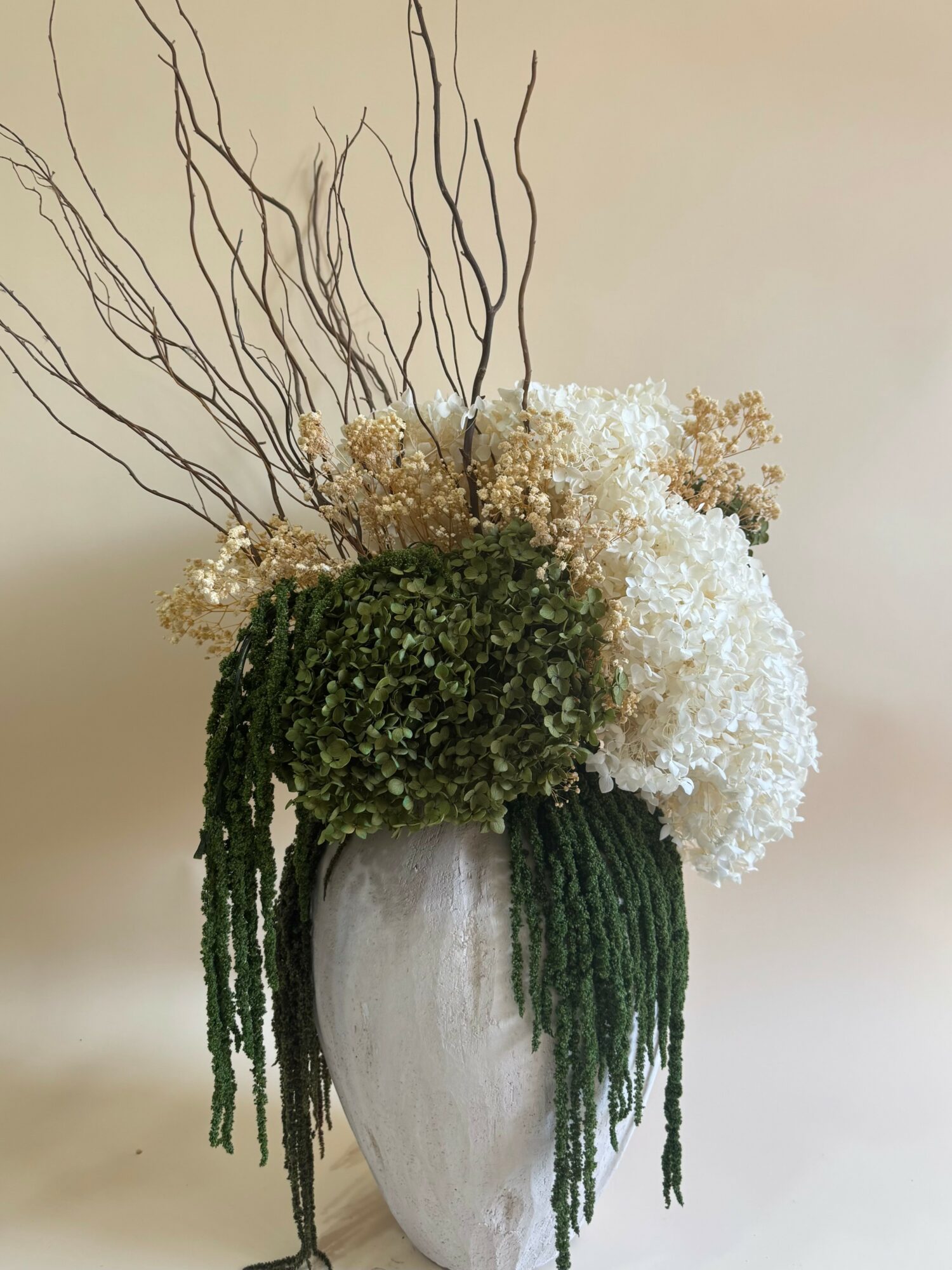 Vase with white, green, and brown dried flowers and branches, on a plain background.