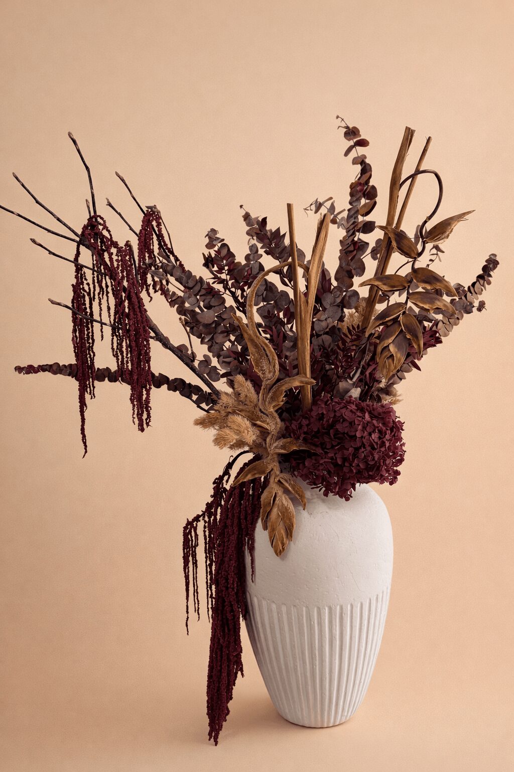 Dried flowers in a white vase against a beige background, including lavender, leaves, and other dried plants.