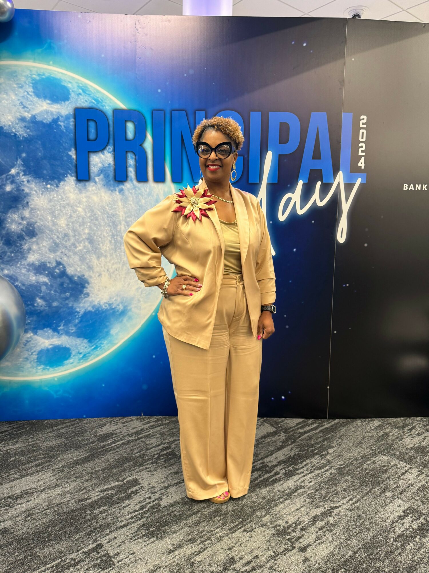 Person in beige suit standing in front of a space-themed backdrop with large blue text reading 'PRINSPAL day'.