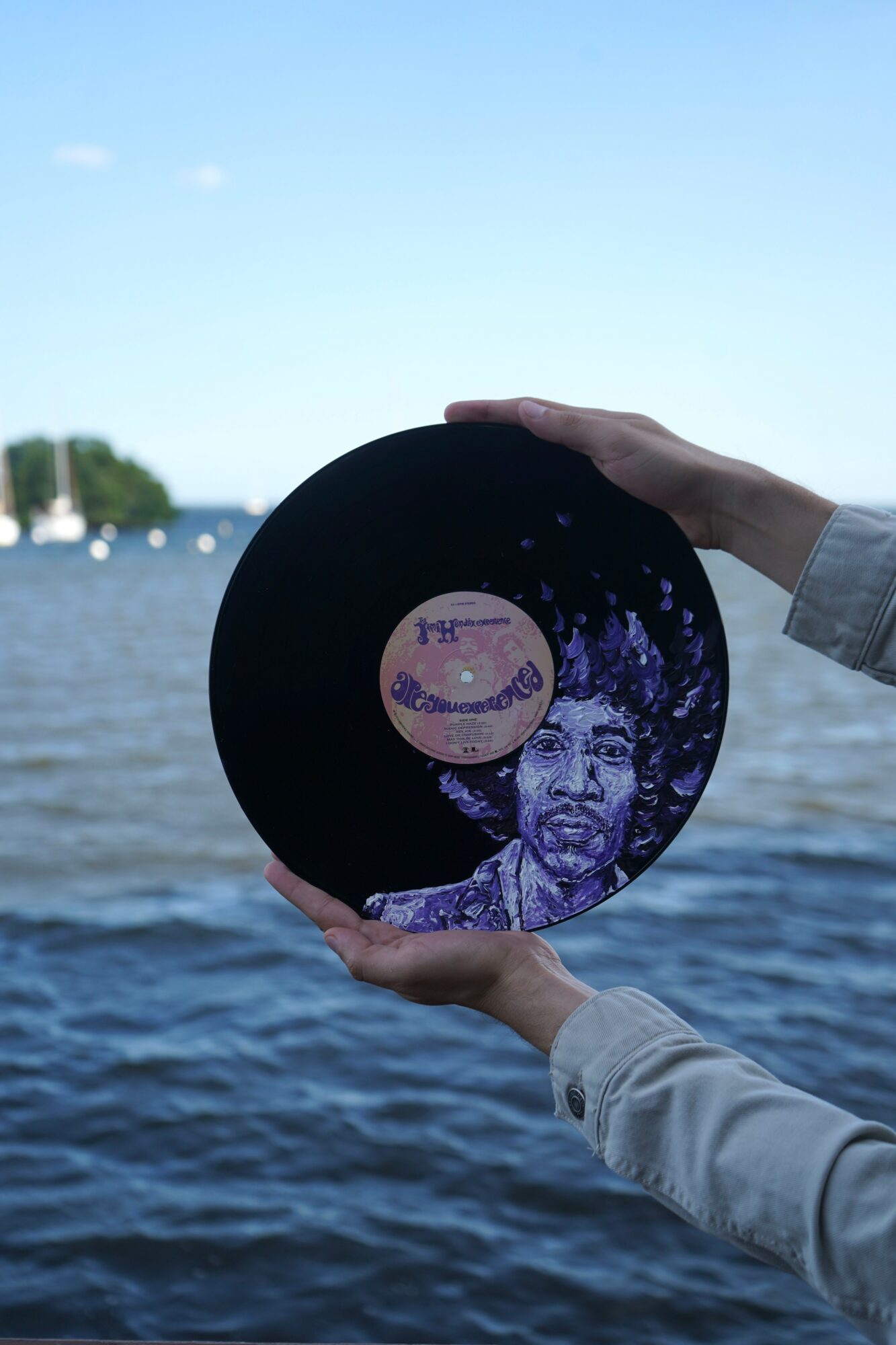 Person holding a black circular object with a purple illustration of a child's face, against a water and sky background.
