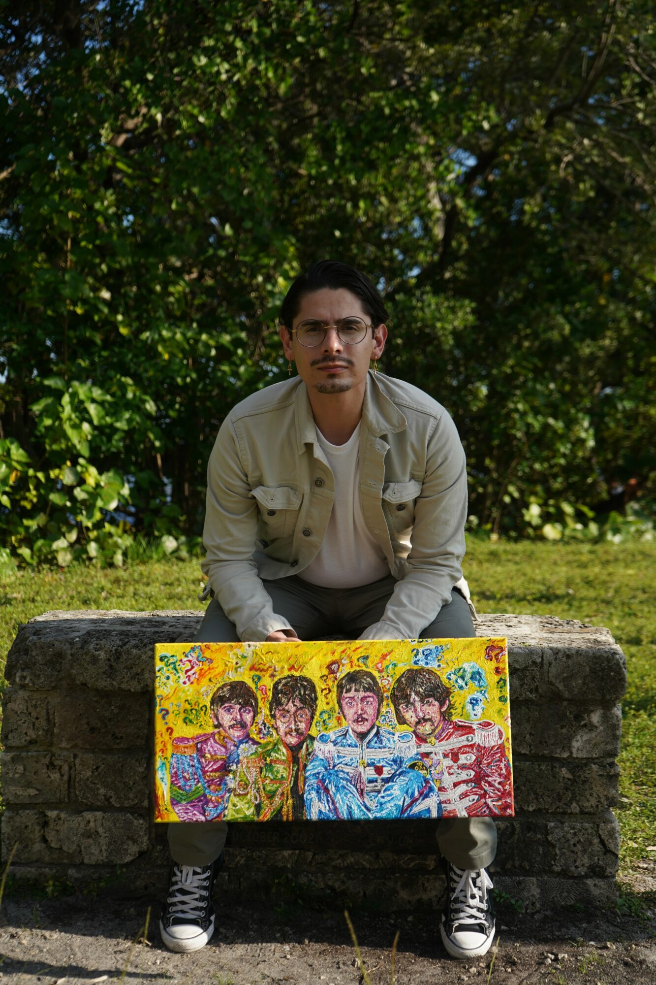 Person crouching behind a colorful painting outdoors with trees in the background.