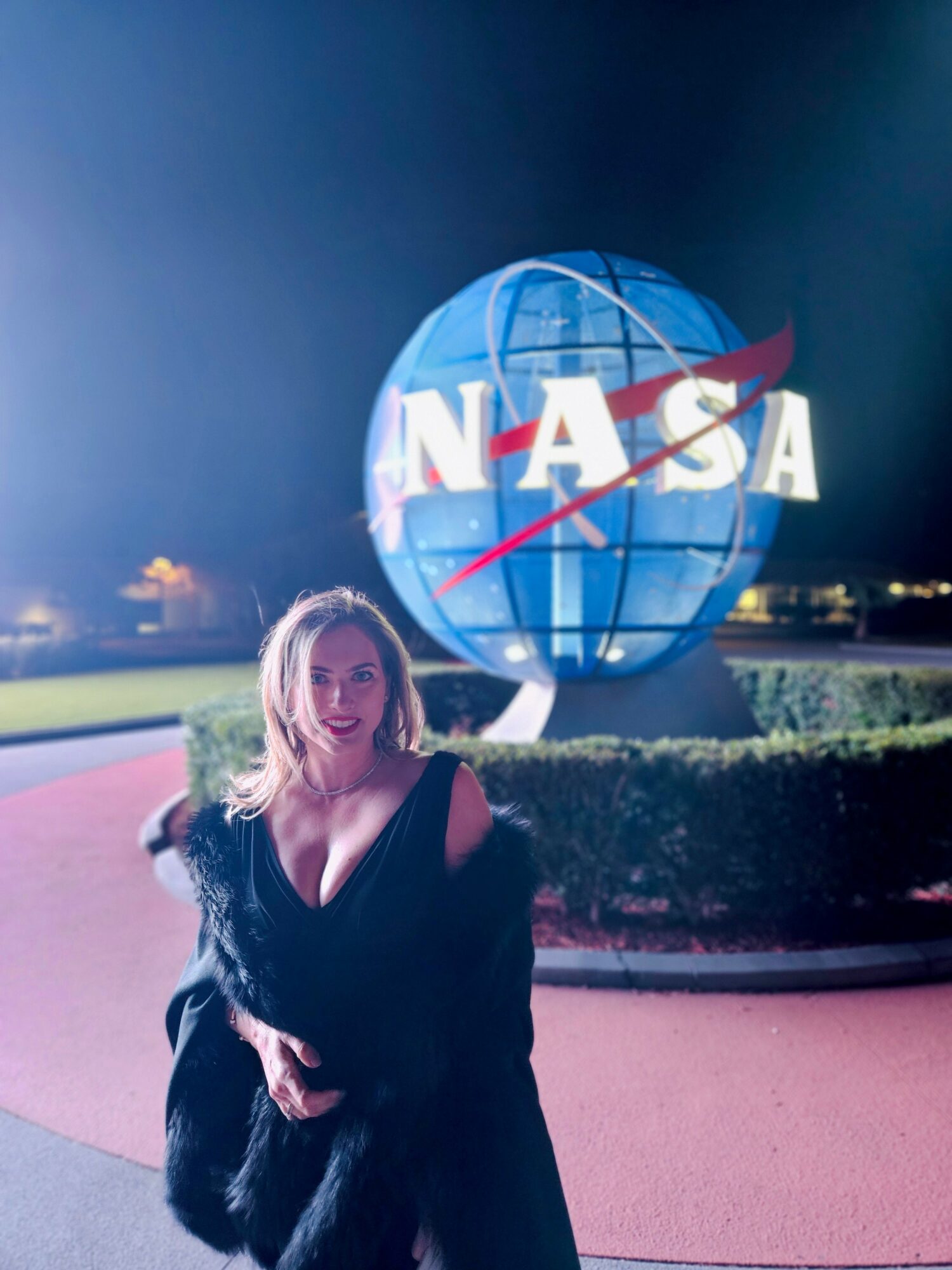 Woman standing in front of NASA logo globe at night, smiling, with a dark sky background.