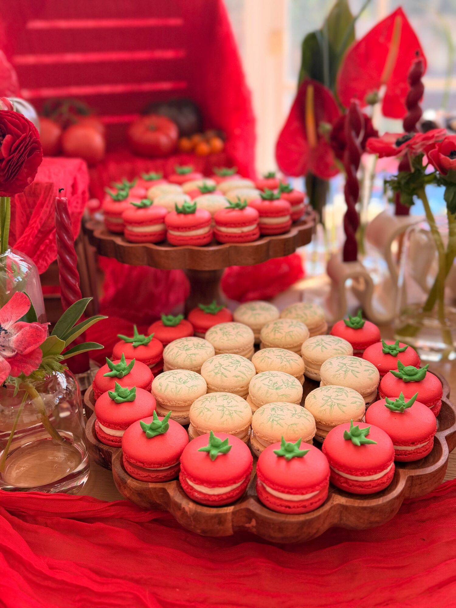 Plate of red and white cookies decorated with green leaves, on a red tablecloth with floral arrangements in the background.