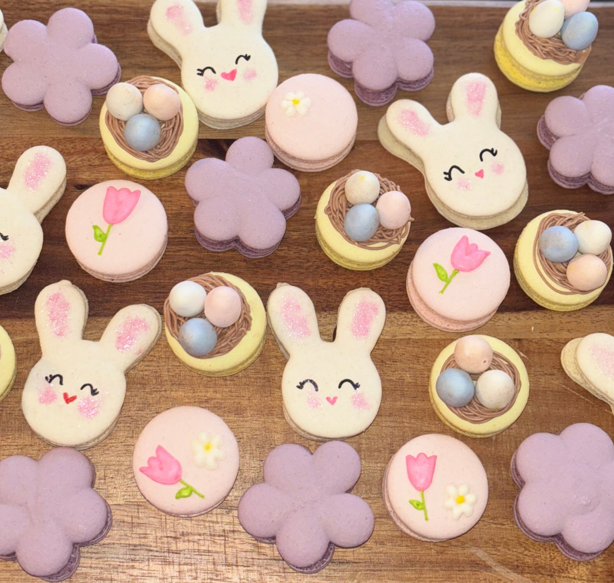 Easter-themed cookies and candies with bunny faces, flowers, and pastel colors on a wooden surface.