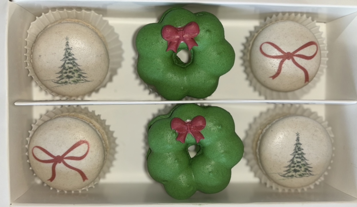 Six holiday-themed cookies in a box, including three with Christmas trees, two with green wreaths and red bows, and one with a red bow.