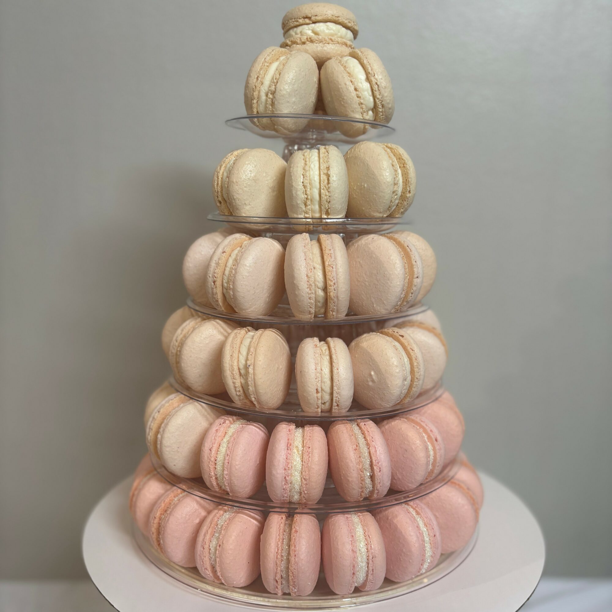 Stacked tiered display of pink and beige macarons on a white stand against a plain background.