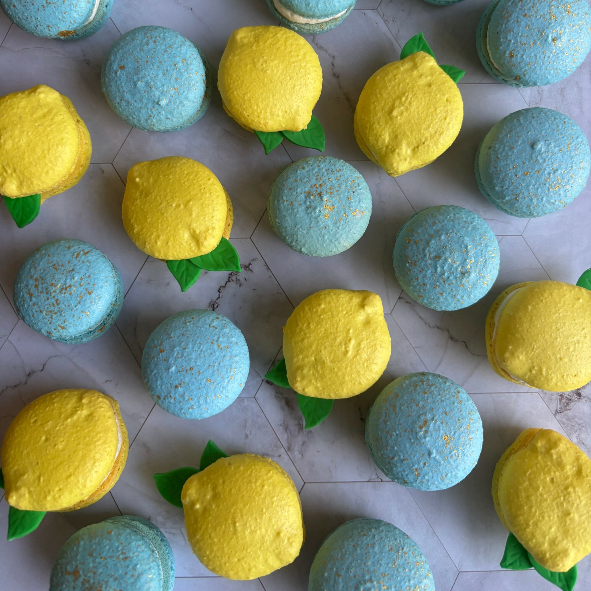 Colorful bath bombs shaped like lemons and blue spheres with green leaves, arranged on a white tiled surface.