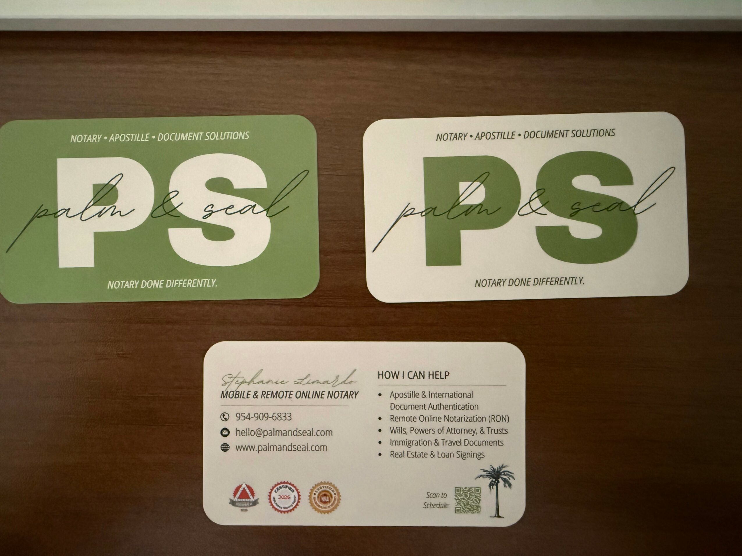 Two rectangular stickers with green and white backgrounds, featuring the letters 'PS' and handwritten text, on a wooden surface.