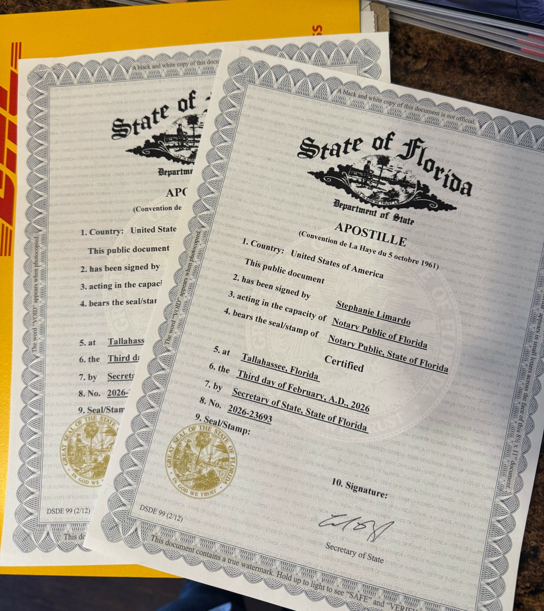 Two Florida apostille certificates with official seals and signatures, overlapping on a surface with a yellow document partially visible behind them.