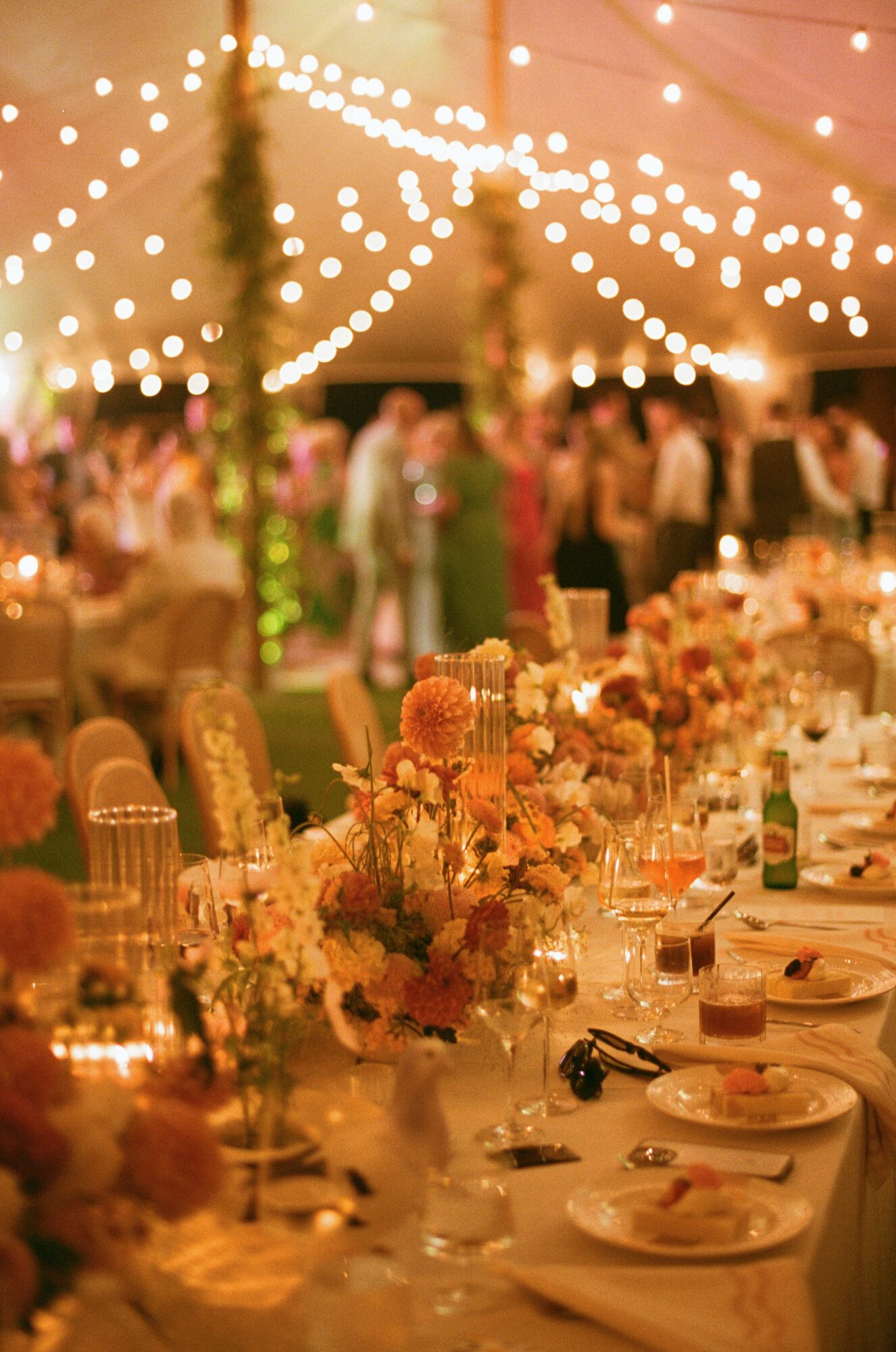 Decorated banquet table with floral centerpieces, plates, and glasses under string lights at a celebration event.