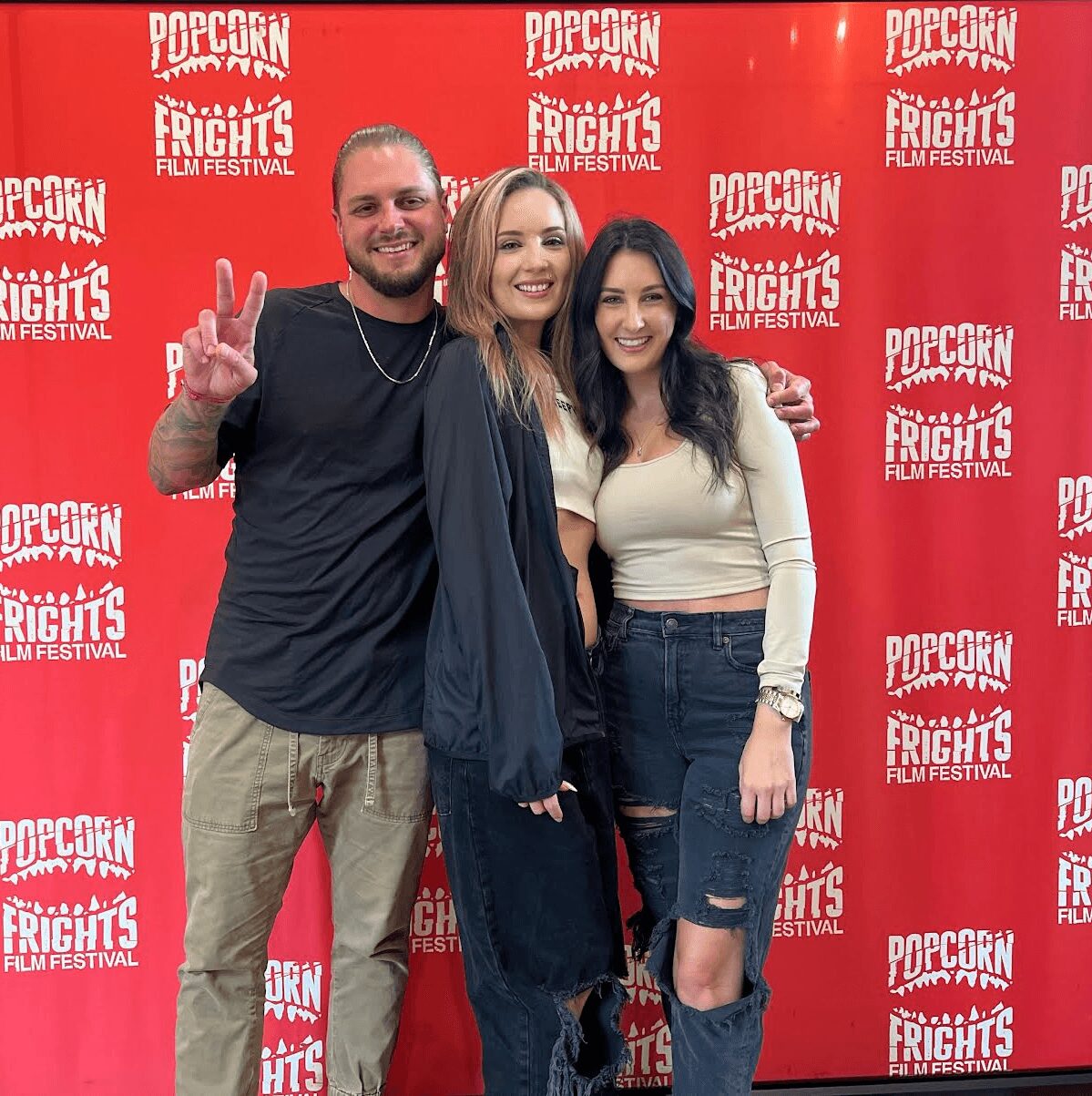 Three people smiling and posing in front of a red backdrop with white text at a film festival.