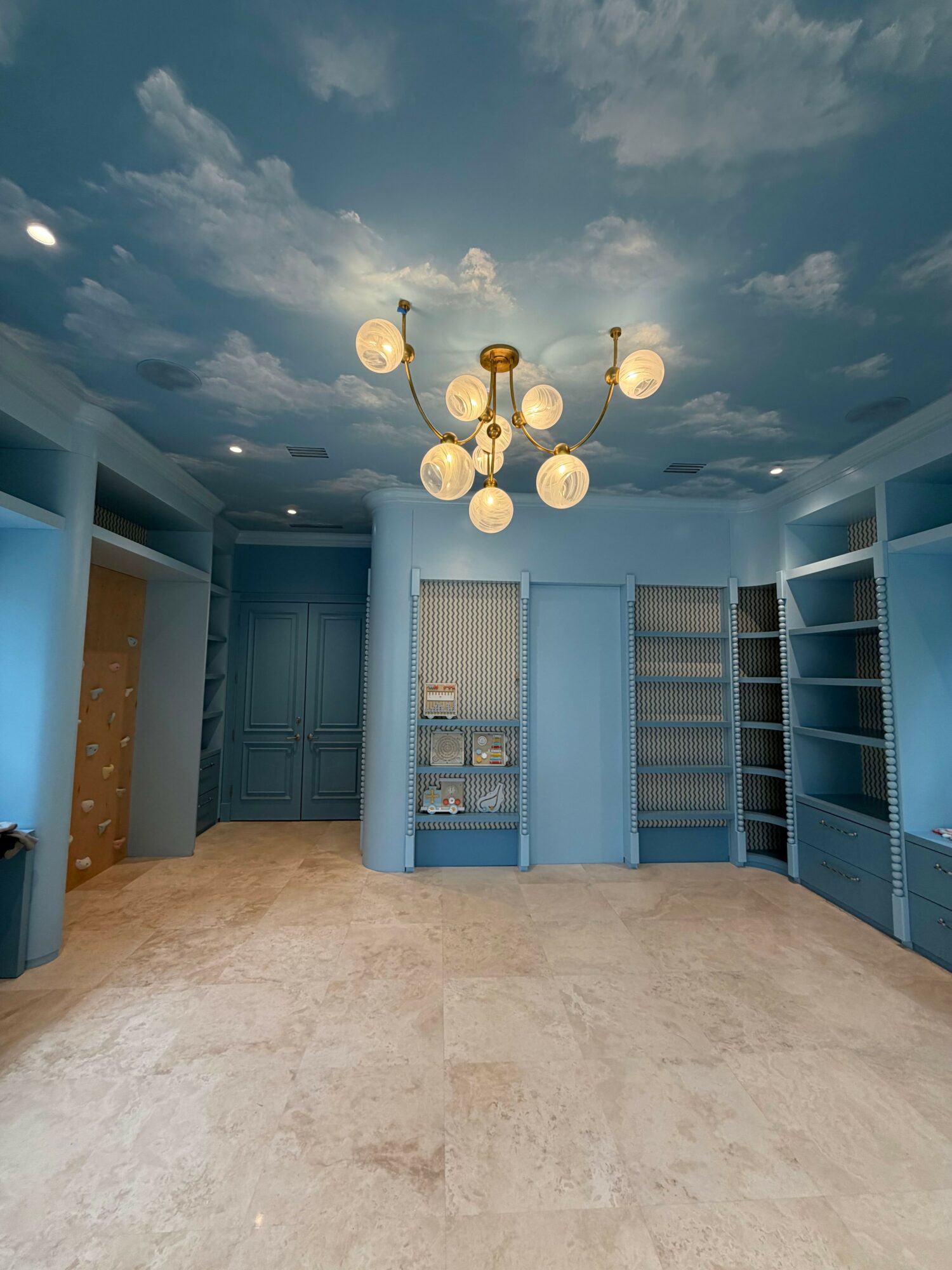 Room with sky and cloud mural ceiling, chandelier, blue walls, and beige carpeted floor.
