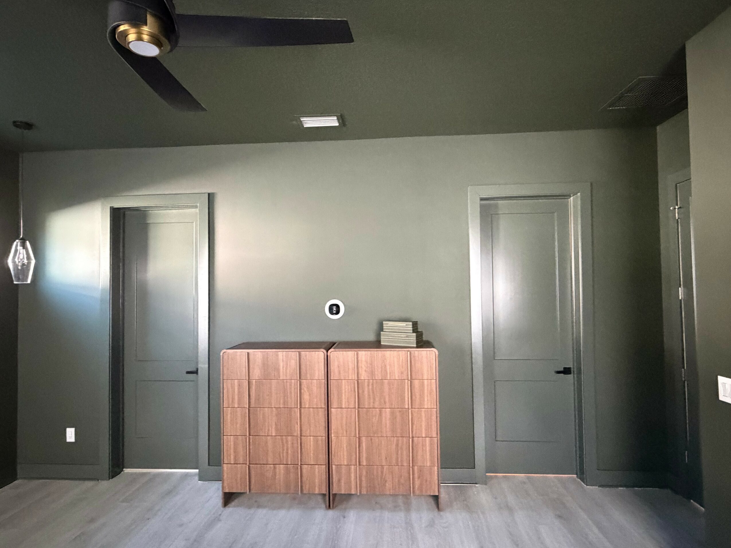 Room with two closed doors, a wooden cabinet, and a ceiling fan, painted in shades of green and gray.