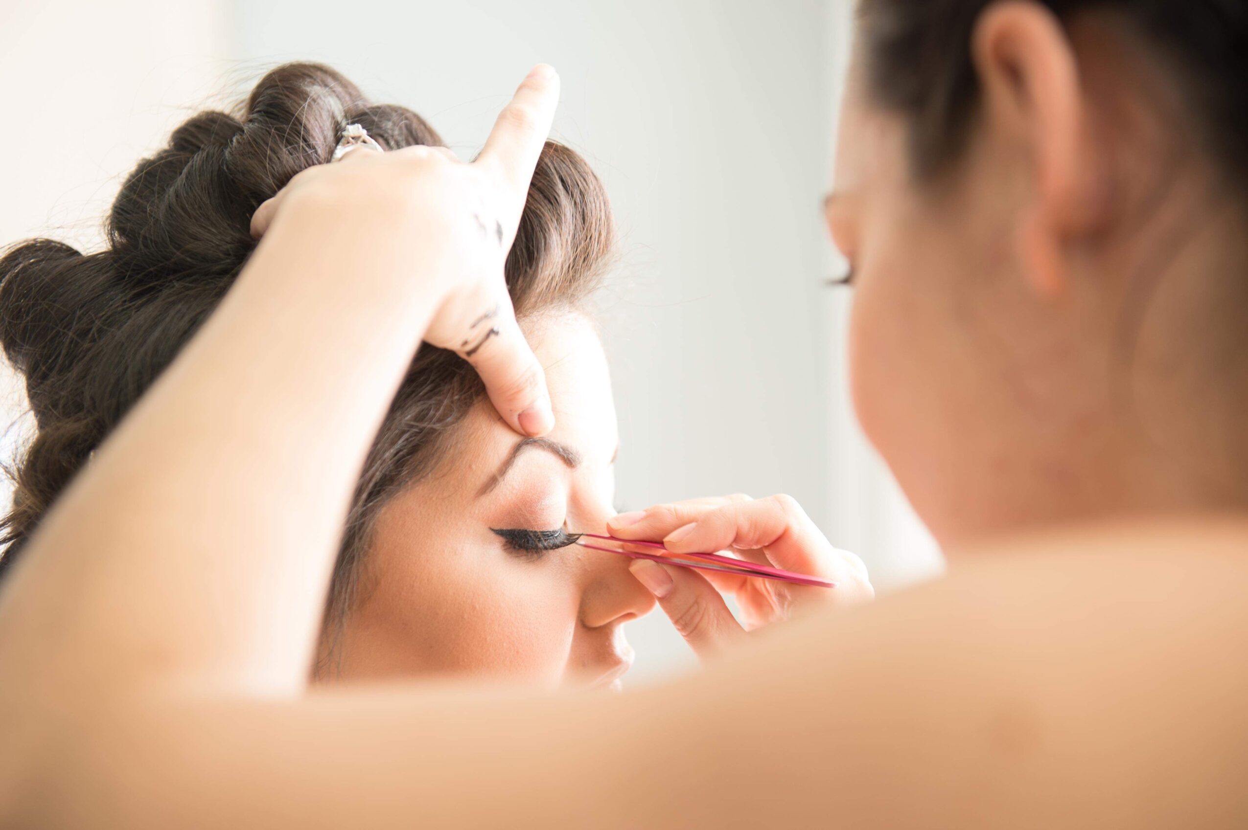 Makeup artist applying eye makeup to a woman with hair held back, focusing on her eye area.