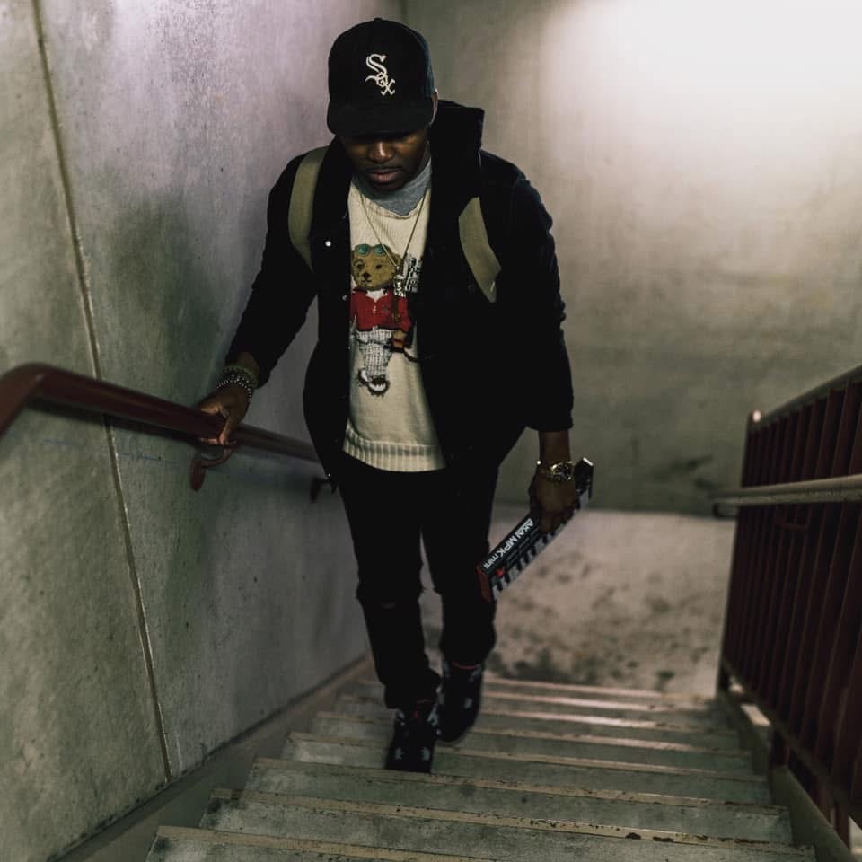 Person walking up stairs with a backpack, wearing a cap, sweater, and dark pants, holding a book or folder.