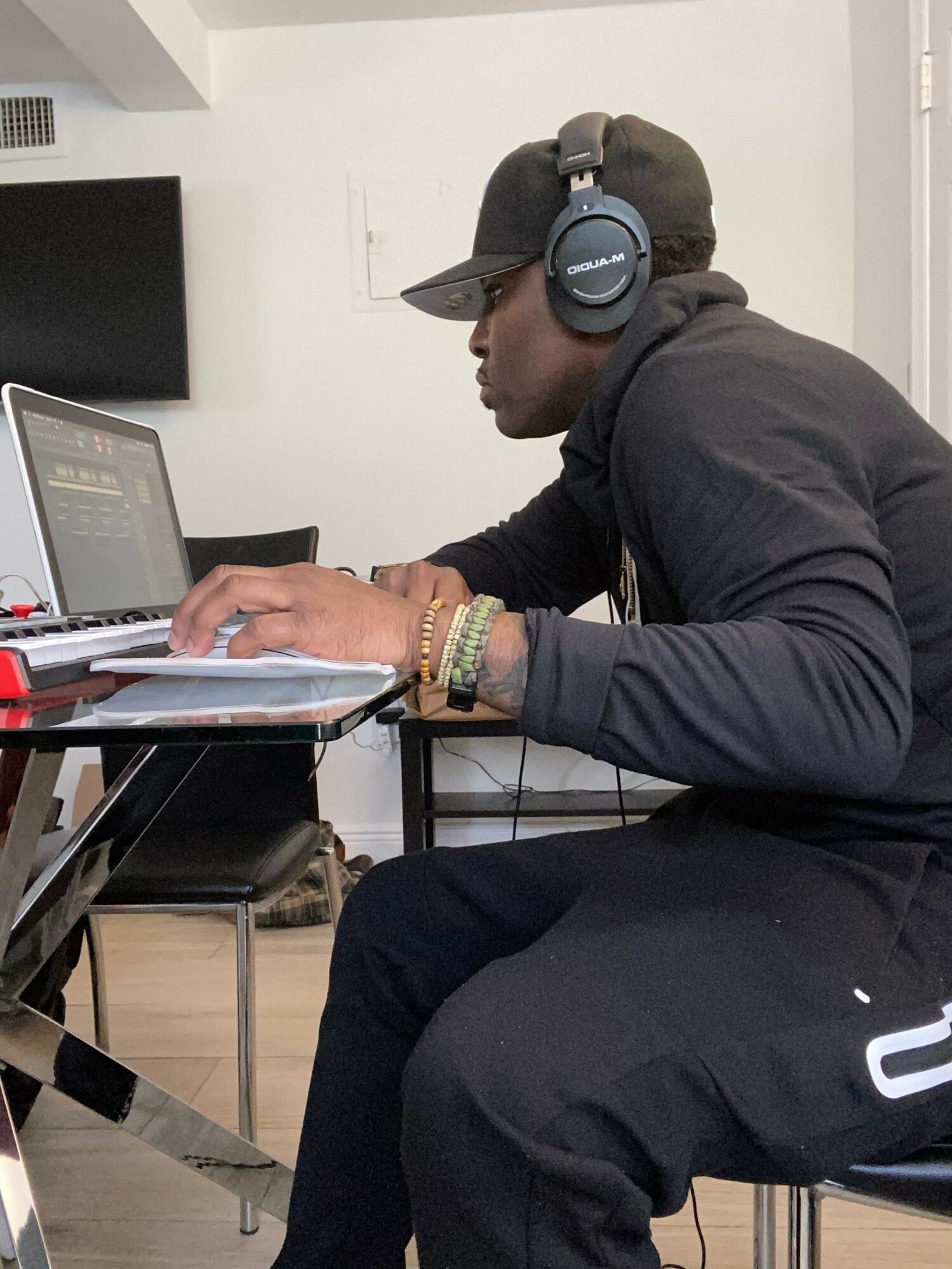 Person wearing headphones, black cap, and dark clothing, working on a laptop at a desk.