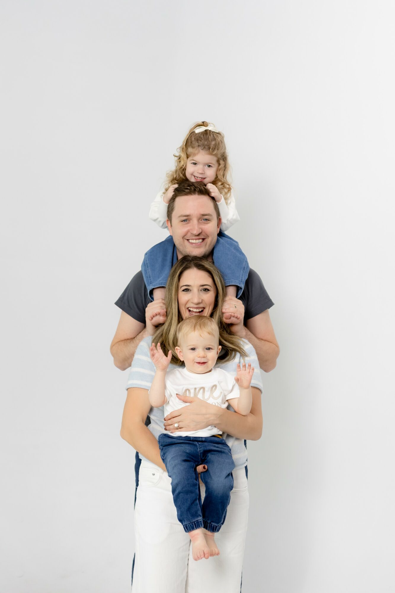 A man with three children, one on his shoulders and two in front, smiling and standing against a plain white background.