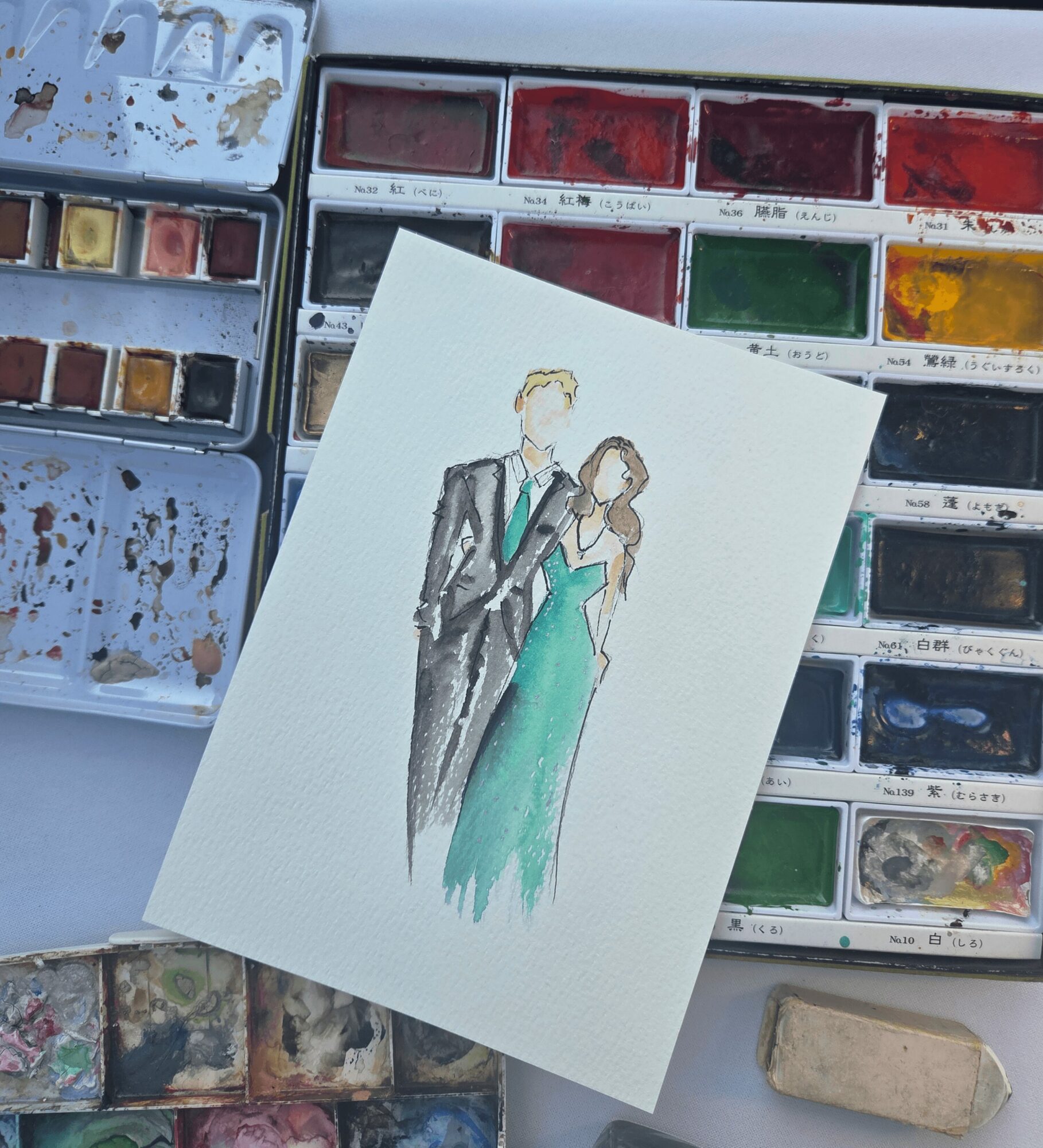 Watercolor painting of a man and woman in formal attire embracing, with watercolor palettes in the background.