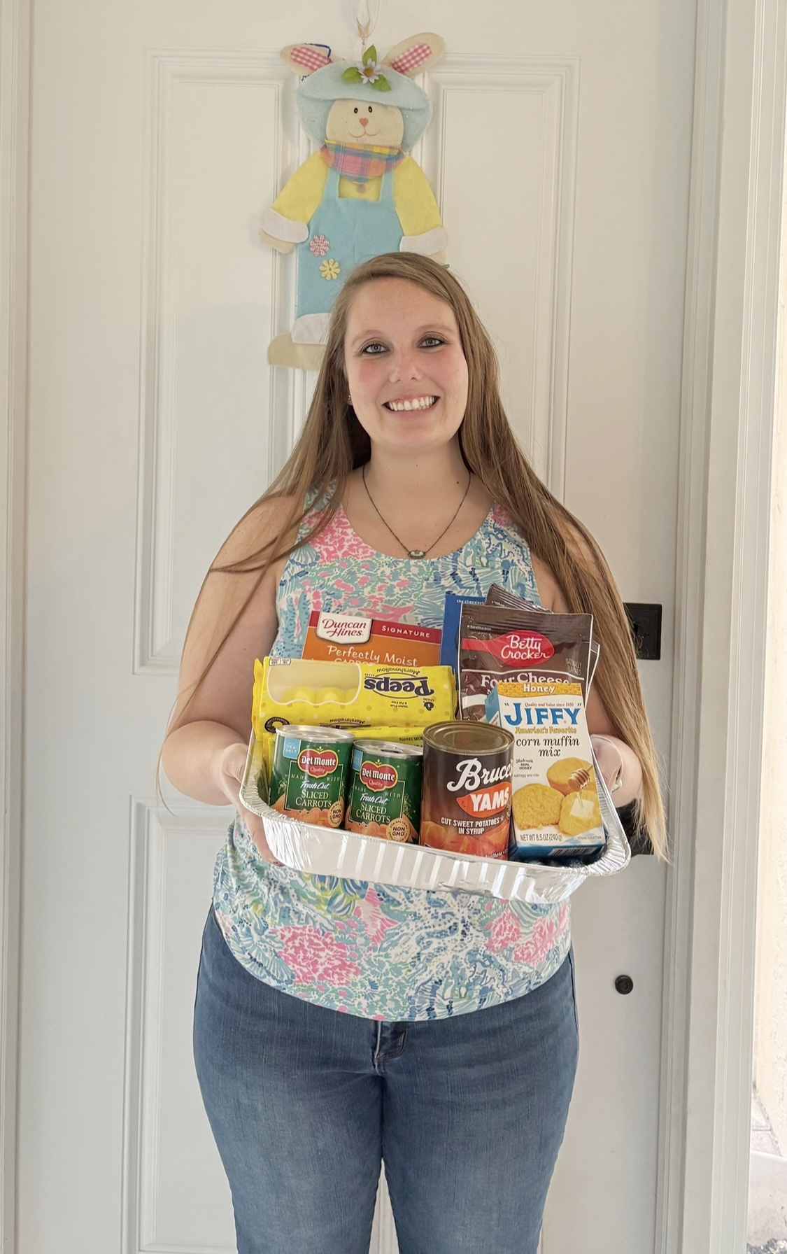 Young girl holding a basket of snacks and drinks, standing in front of a door with a decorative hanging.
