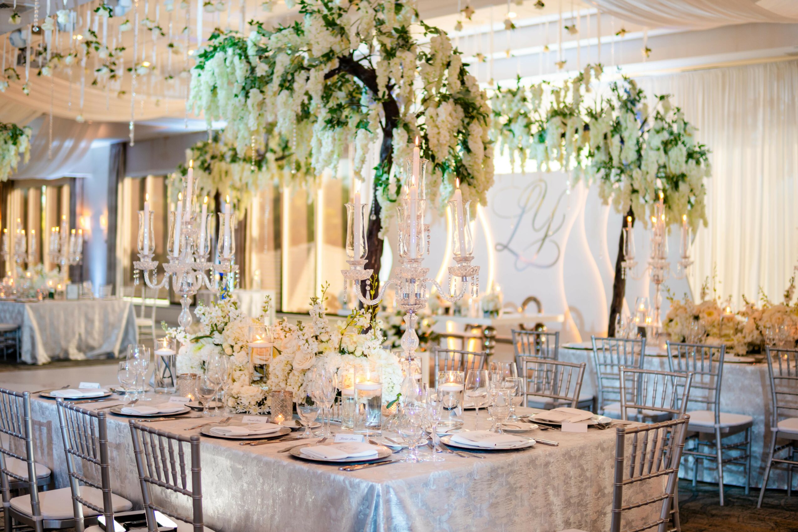 Elegant banquet table with floral centerpiece, candles, and tableware in a decorated event space.