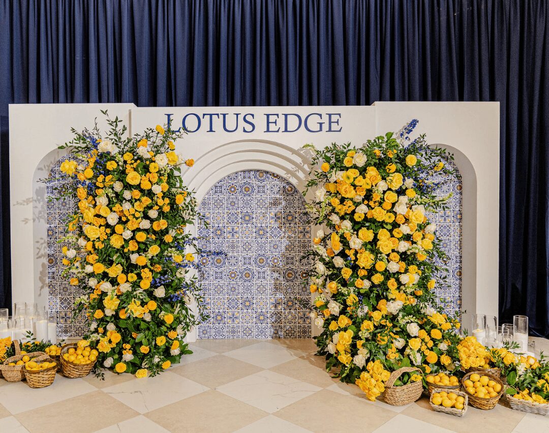 Decorative backdrop with yellow flowers, blue accents, and a sign reading 'LOTUS EDGE' on a stage with dark curtains.