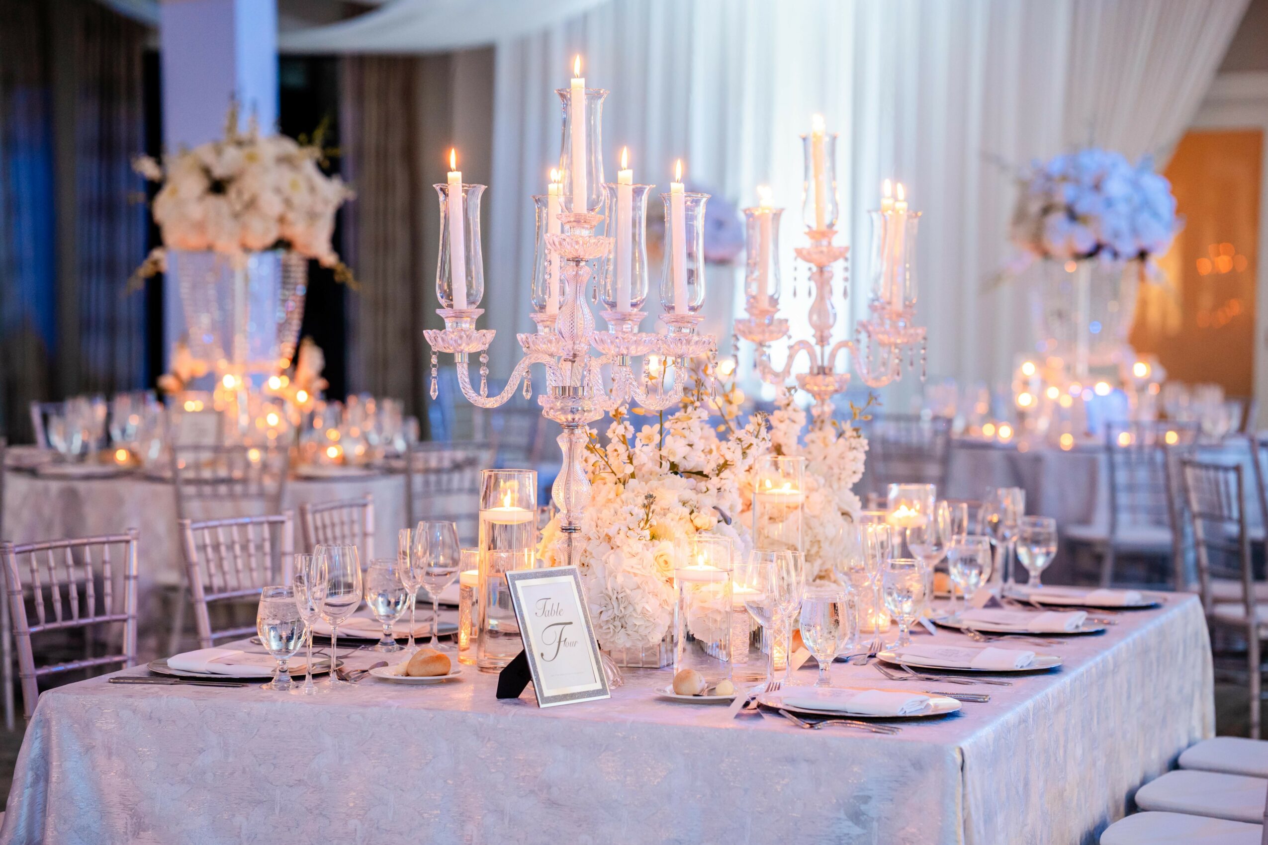 Elegant banquet table with a large candelabrum, floral arrangements, and candlelit decor in a decorated event space.
