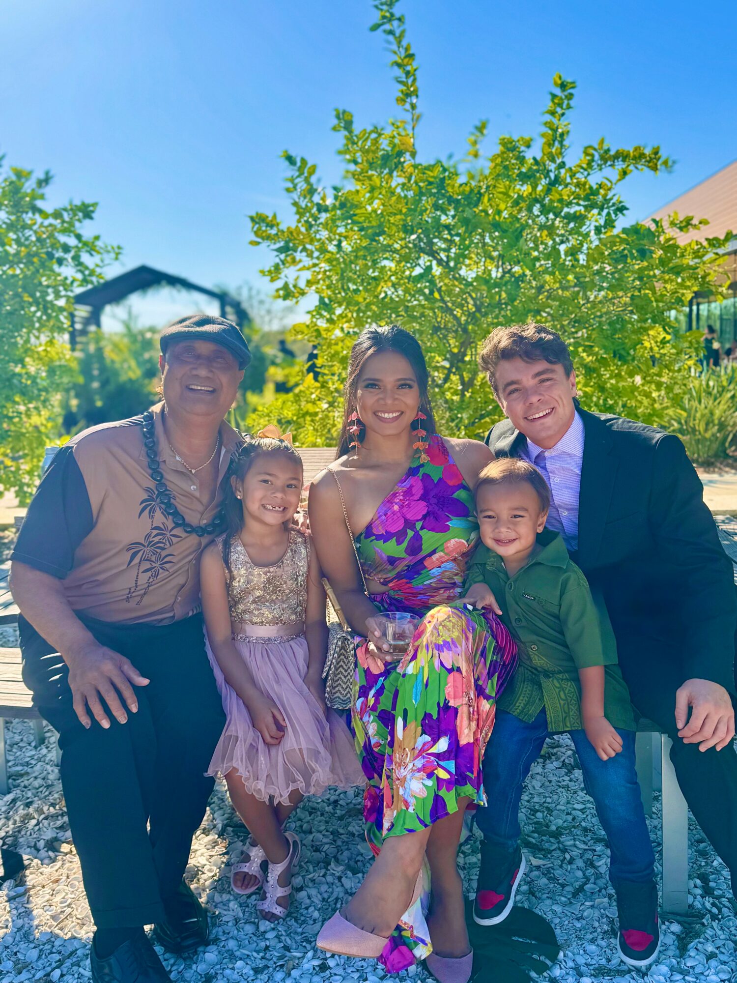 Group of five people outdoors, standing in front of a tree and blue sky, smiling for the photo.