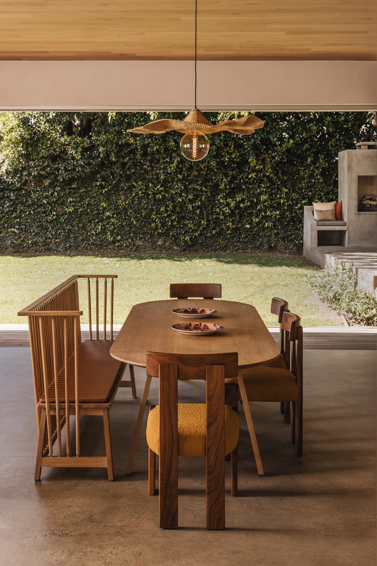 Dining table with six chairs in a room with large window showing outdoor greenery.
