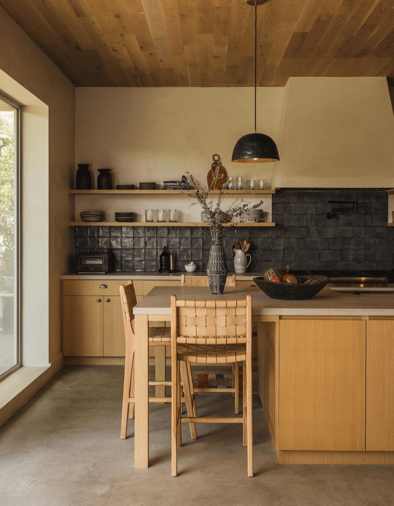 Kitchen with wooden cabinets, a black pendant light, a vase with branches, and a sliding glass door on the left.