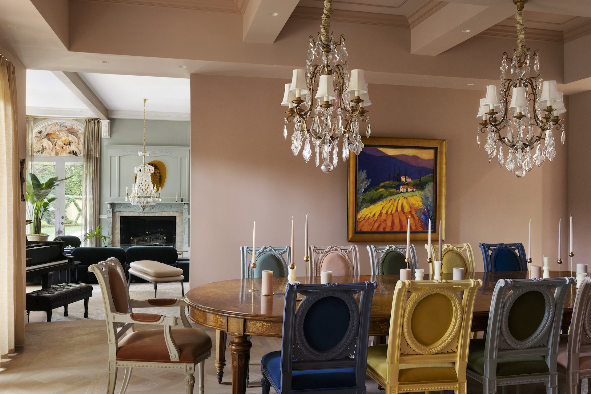 Elegant dining room with chandelier, colorful chairs, and a landscape painting on the wall.