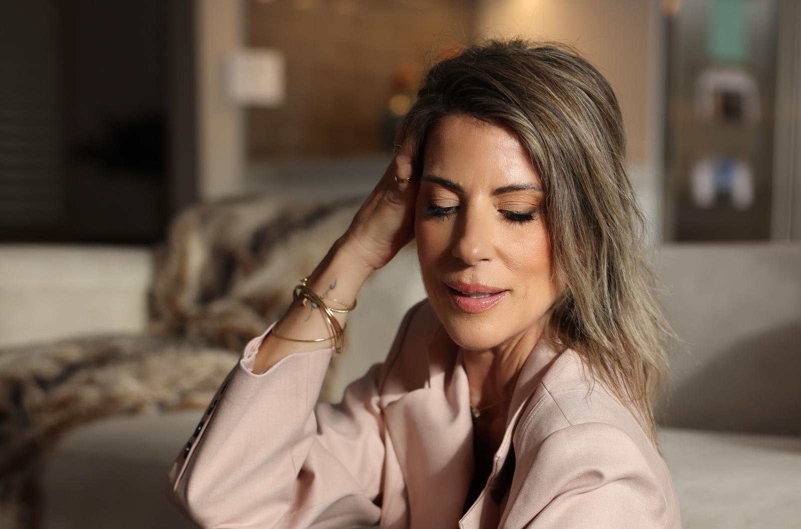 Woman with shoulder-length hair, eyes closed, resting her head on her hand, sitting indoors with a blurred background.