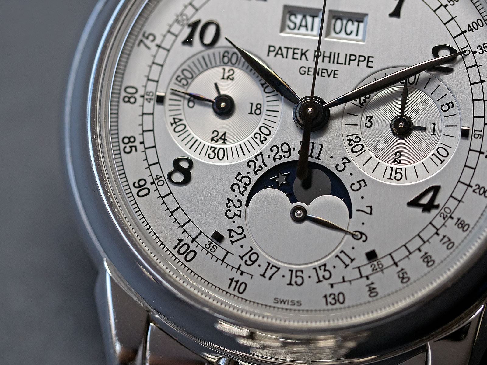 Close-up of a Patek Philippe watch face with multiple dials, date, and moon phase, showing time 10:09:36.