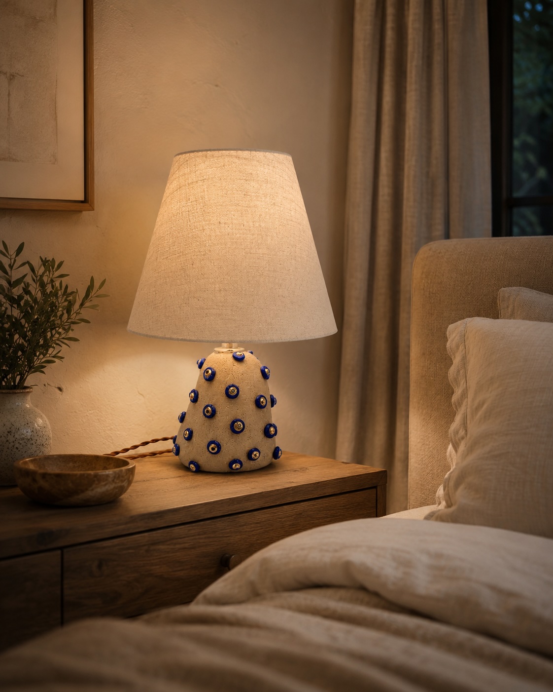 Table lamp with a white shade and a base decorated with blue and white circular patterns on a wooden nightstand, beside a bed.