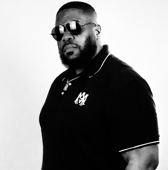 Man with sunglasses and beard wearing a black polo shirt, facing slightly to the right, against a plain background.