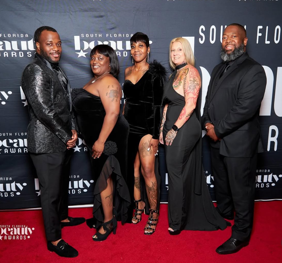 Five people in formal attire pose on red carpet at awards event, backdrop displays event branding.