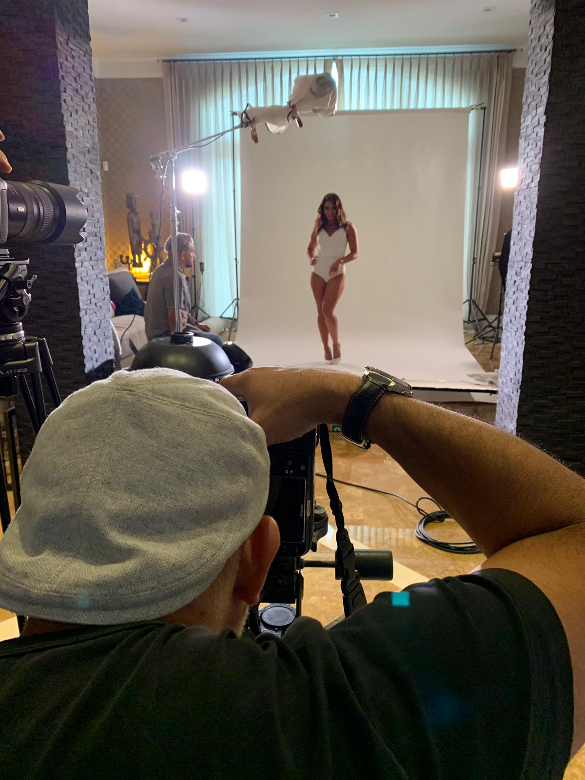 Photographer taking picture of a woman in a white dress on a white backdrop in a studio.