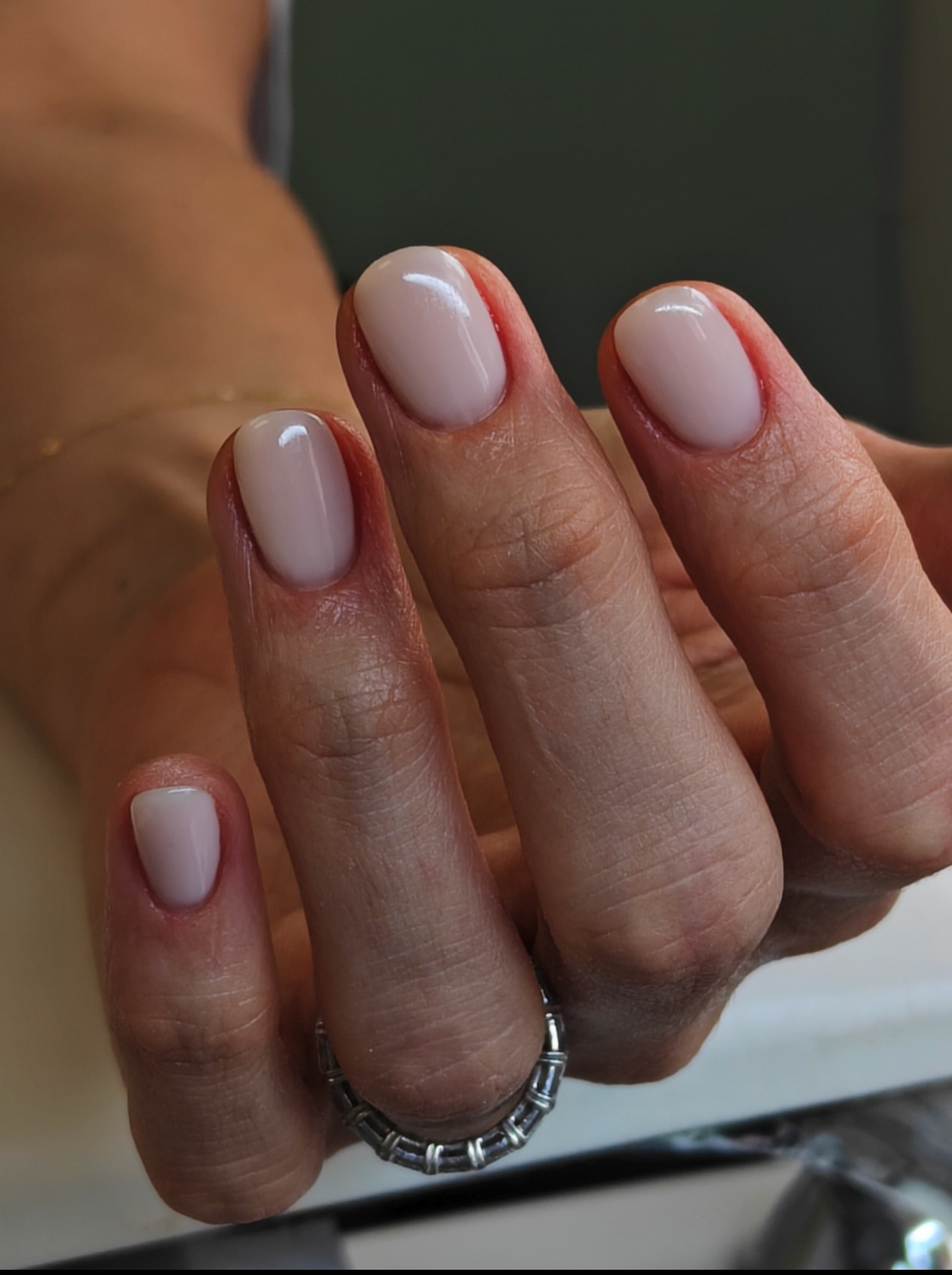 Close-up of a hand with neatly manicured nails painted in light pink, wearing a silver ring on the ring finger.