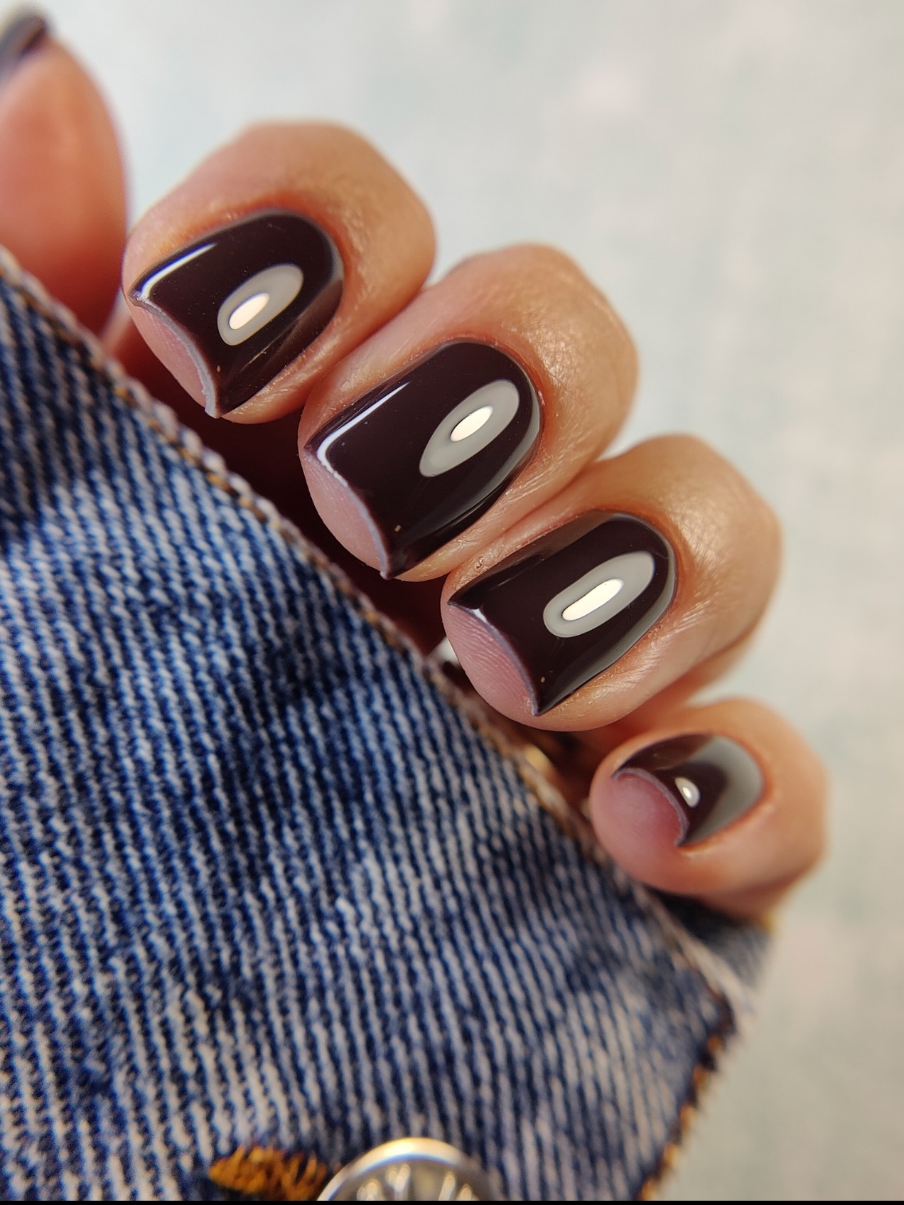 Close-up of four fingers with dark, glossy nail polish, partially covered by denim fabric